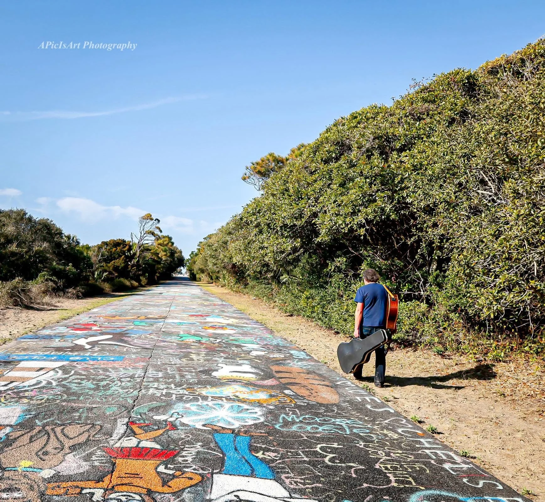 Jamie Dose walking with a guitar along an art-covered road